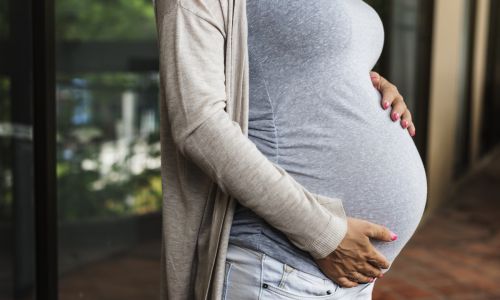 Profile view of a pregnant woman with her hands rested on her stomach